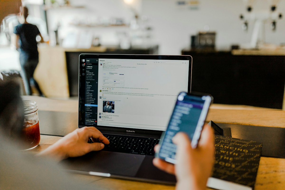 A person using a laptop and phone at a cafe table