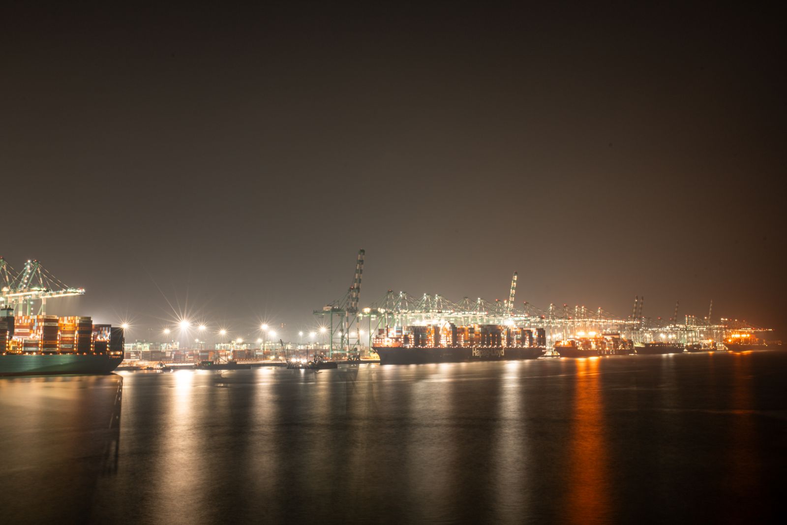 Un puerto de contenedores de noche, con grúas y buques iluminados sobre el agua oscura